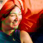 A woman is lying with her head on a man's chest, both smiling at each other