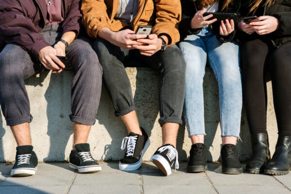 people sitting on a wall looking at their phones 