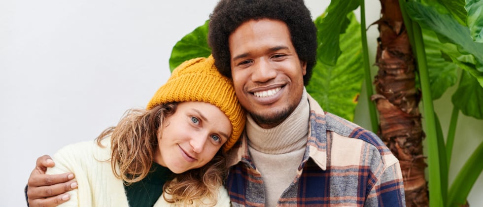 A woman sitting next to a man. She leans her head on his shoulder, he is laying his hand around hers.