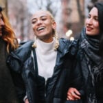 Three women walk together through the city arm in arm as a symbol of Polymory