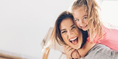 Single parent dating symbolized by mother carrying her child on her back and laughing into camera
