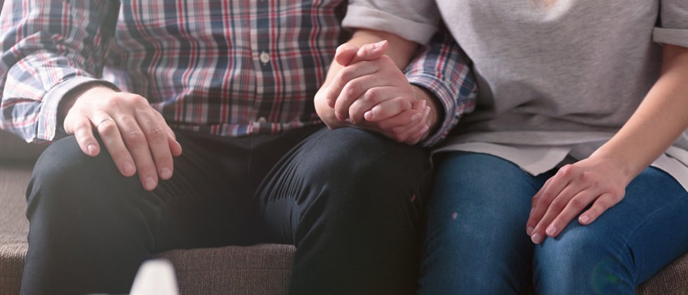 A couple sitting other with their hands held together resting in their lap