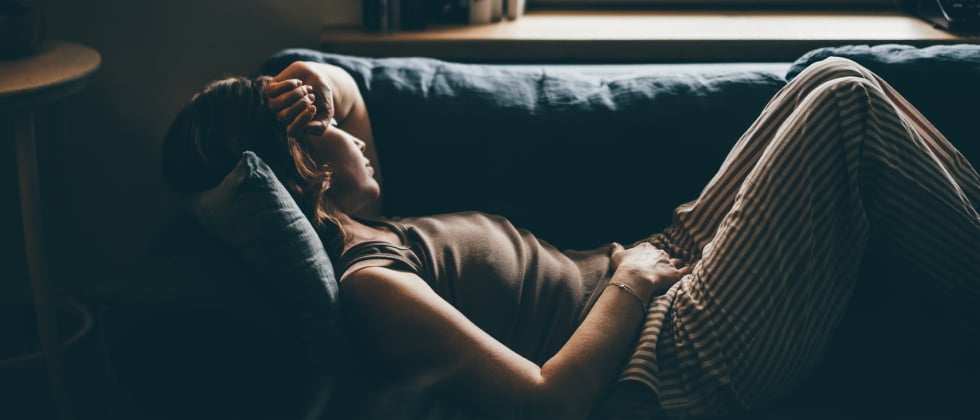 A sad woman laying on the couch, wondering why breakups hurt so much