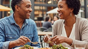 A couple is smiling at each other and enjoying food on a market.