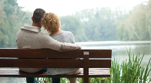 A couple is sitting on a bench in front of a lake.