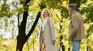 A couple on a walk in the park next to green trees.