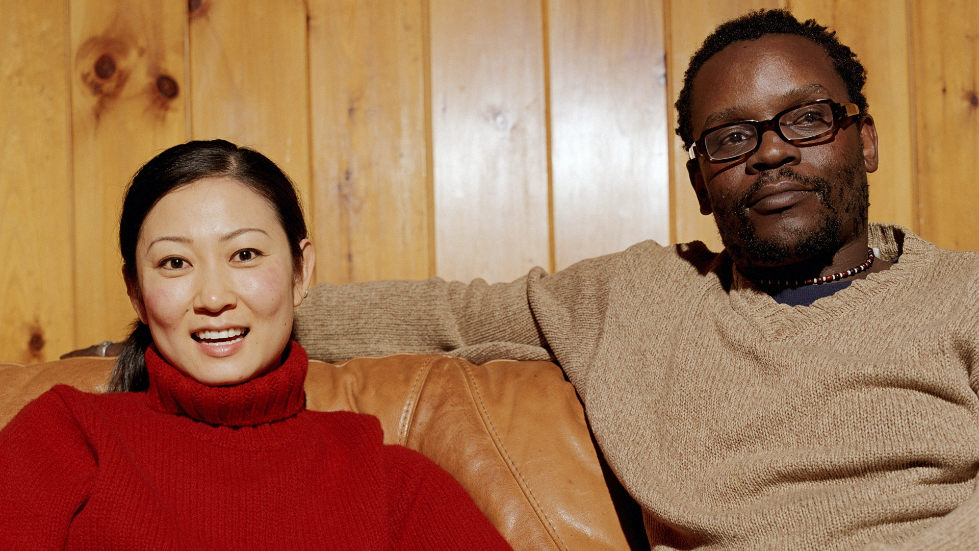An Asian woman and a black man are sitting on a sofa enjoying a conversation.