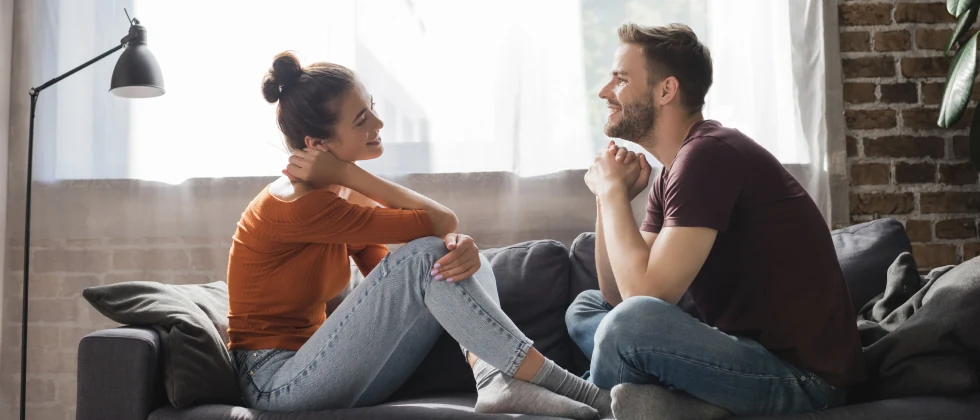 A couple are sitting together on the couch and talking.