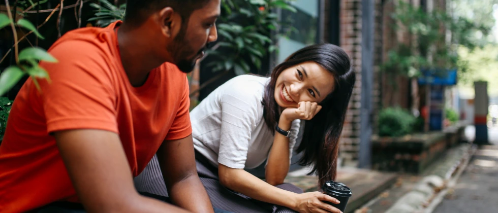 A woman and a man sitting, chatting and smiling at each other, showing how to get a guy to ask you out