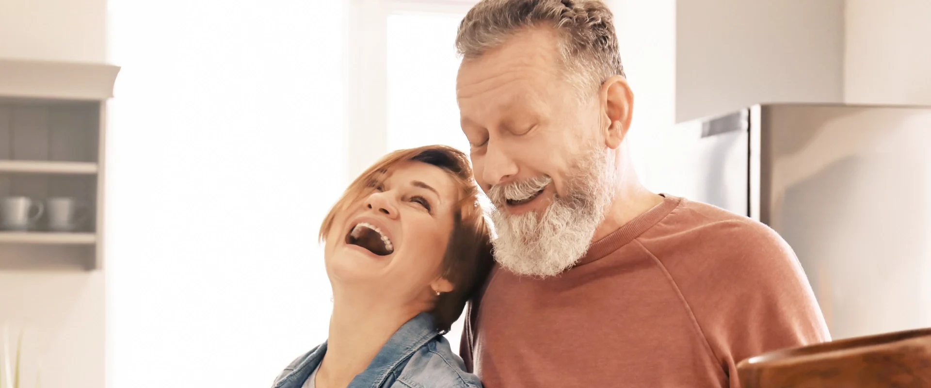 Mature couple laughing together at home in the kitchen.